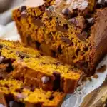 Closeup of moist pumpkin chocolate chip bread with gooey chocolate chips and golden-orange crumb, sliced on parchment and wood board.