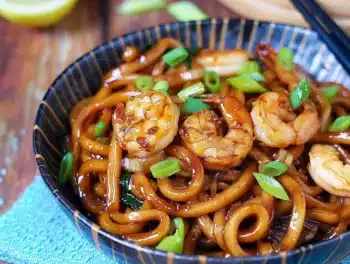 Close-up of delicious Yaki Udon with shrimp garnished with chopped spring onions in a patterned bowl